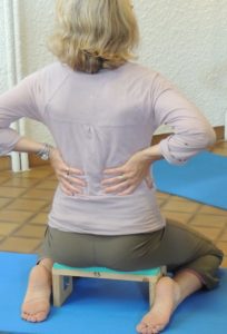 Assis sur un petit banc, mains posées sur les côtes dans le dos, pour apprendre à respirer. Yoga Yvette Clouet